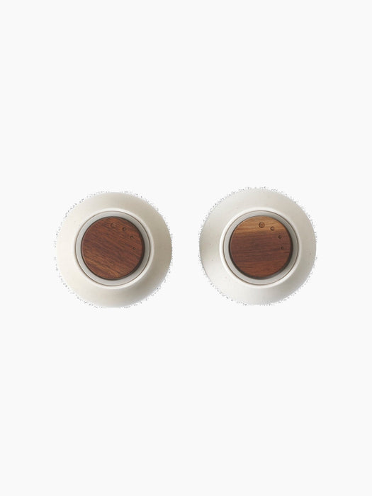 A top-down view of two Audo Bottle Grinders in sand-coloured ceramic, each featuring a dark wood top, on a black background.