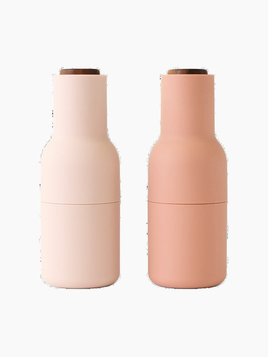 Front view of two Audo Bottle Grinders. One is a light nude pink and the other a darker blush nude, both with dark wood tops.