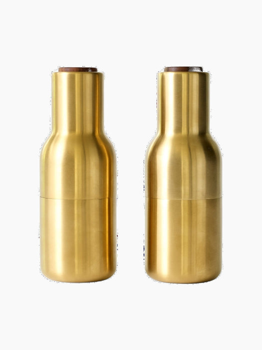 A pair of Bottle Grinders in brushed brass with walnut lids, presented side-by-side against a black background.