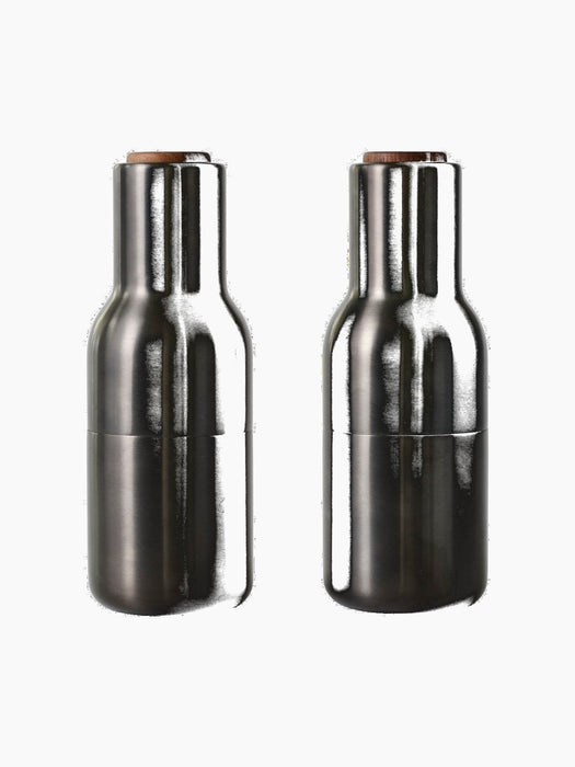 A front view of two Bottle Grinders made from bronzed brass with walnut lids, set against a black background.