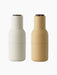 A pair of Audo Bottle Grinders, one barley and one off-white, both with dark walnut wood lids. Shot on a black background.