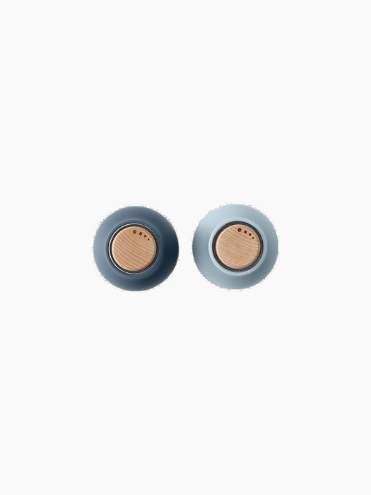 A top-down view of two Small Bottle Grinders. The left is dark blue and the right is light blue, both with round wooden lids.