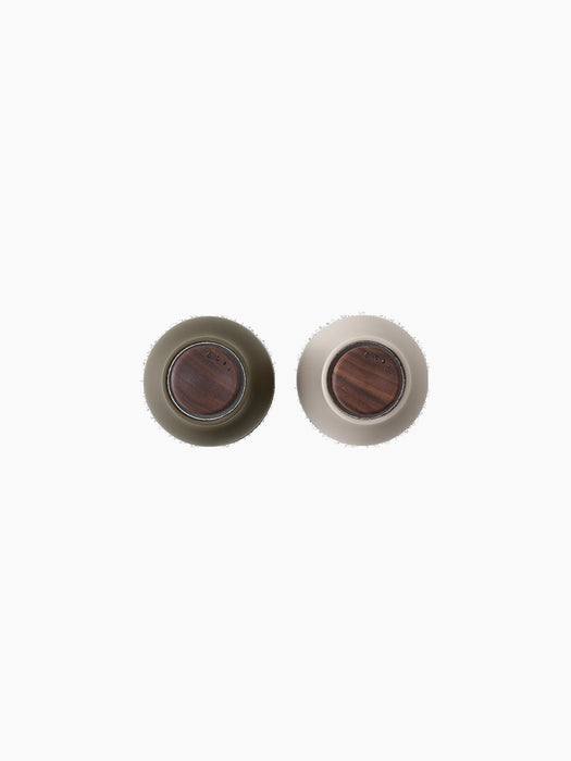 Top-down view of two Bottle Grinders with walnut lids on a black background. One is hunting green and the other is beige.