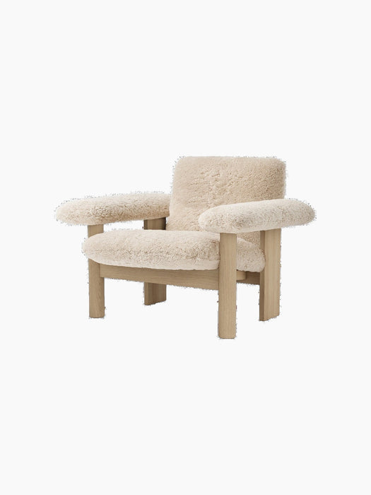 A three-quarter view of the Brasilia Lounge Chair, Low Back, featuring a natural oak frame and plush, off-white sheepskin.
