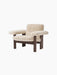Angled view of the Brasilia Lounge Chair in cream sheepskin with a dark stained oak frame, shown against a black background.