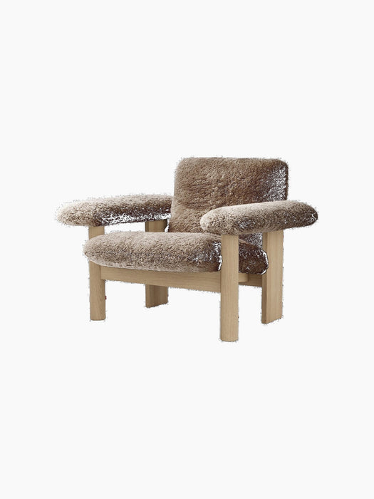The Brasilia Lounge Chair, Low Back, in brown sheepskin with a natural oak frame, shown at an angle on a black background.