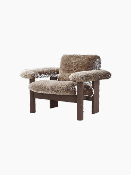 Angled view of the Brasilia Lounge Chair, Low Back, upholstered in plush brown sheepskin with a dark stained wood frame.