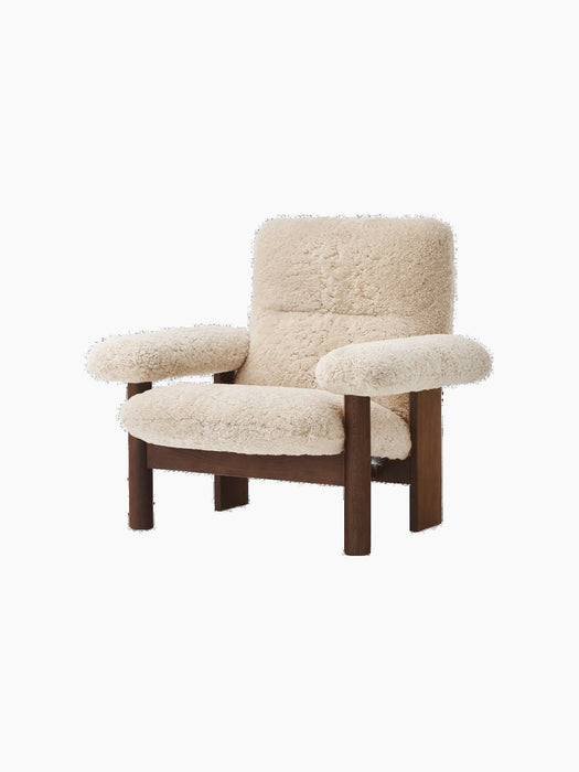 An angled view of the Brasilia Lounge Chair, high back, featuring a dark stained oak frame and plush off-white sheepskin.