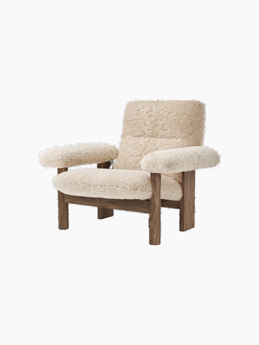 Angled view of the Brasilia Lounge Chair, featuring a high back and cushioned seat in natural sheepskin and a walnut frame.