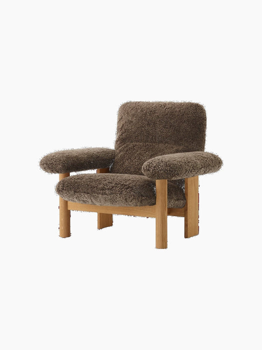 The Brasilia Lounge Chair with a natural oak frame and Root sheepskin upholstery, seen from an angle on a black background.