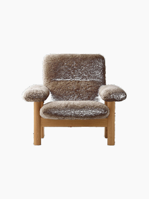 Front view of the Brasilia Lounge Chair with a natural oak frame and thick brown sheepskin upholstery on a black background.