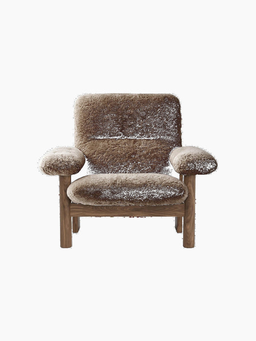 The Brasilia Lounge Chair, High Back, shown front-on. It has a dark wood frame and is upholstered in plush, brown sheepskin.