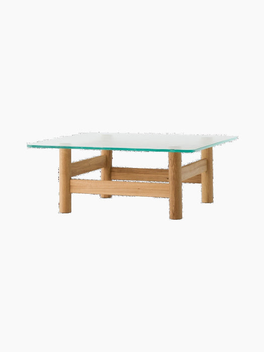 Brasilia Lounge Table, shown from a side angle, with a square glass top and a solid natural oak base on a black background.