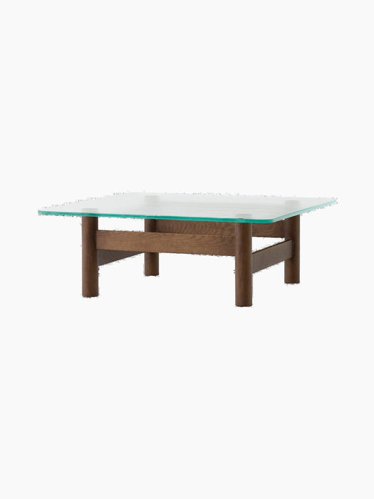 Side view of the Brasilia Lounge Table, featuring a square glass top with rounded corners resting on a dark wood base.
