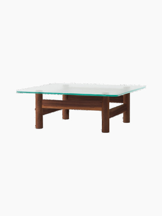 The Brasilia Lounge Table in walnut, seen from an angle. A square glass top rests on a sturdy, four-legged solid wood base.