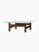 The Brasilia Lounge Table in walnut, seen from an angle. A square glass top rests on a sturdy, four-legged solid wood base.