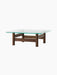 A front-angle view of the Brasilia Lounge Table, featuring a dark wood base with four stout legs and a square glass top.