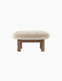 Back view of the Brasilia Ottoman, featuring a plush, cream sheepskin cushion on a wooden base with four cylindrical legs.