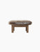 A front view of the Brasilia Ottoman, featuring a plush, brown sheepskin top and four robust, light-toned wooden legs.