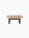 Front view of the Brasilia Ottoman, Sheepskin, featuring a plush, off-white cushion and four robust, cylindrical wooden legs.