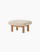 Angled view of the Brasilia Ottoman with a plush, off-white sheepskin cushion and four cylindrical legs in natural oak.