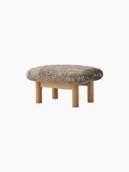 The Brasilia Ottoman, featuring a plush Sheepskin Nature cushion on a solid natural oak frame with four robust legs.