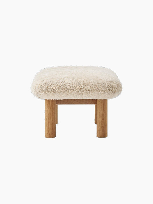 Side view of the Brasilia Ottoman, featuring a Sheepskin Nature cushion on a natural oak frame with robust cylindrical legs.