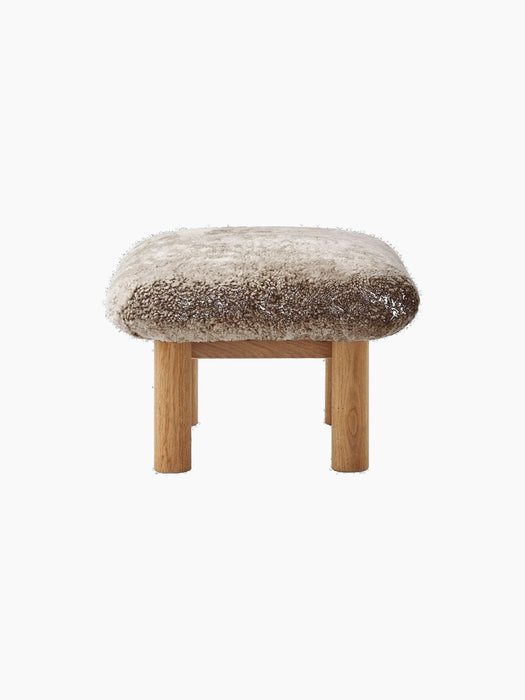 Side view of the Brasilia Ottoman with a plush natural sheepskin cushion and cylindrical natural oak legs.