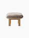 Side view of the Brasilia Ottoman with a plush natural sheepskin cushion and cylindrical natural oak legs.