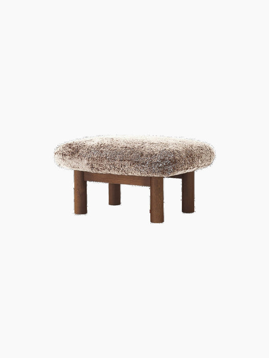 Brasilia Ottoman with a plush 'Root' sheepskin cushion and a dark stained oak frame with four robust, cylindrical legs.