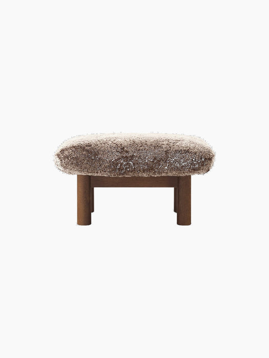 Front view of the Brasilia Ottoman with a dark stained oak frame, cylindrical legs and a fluffy Root sheepskin cushion.