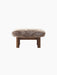 Front view of the Brasilia Ottoman with a dark stained oak frame, cylindrical legs and a fluffy Root sheepskin cushion.