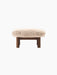 The Brasilia Ottoman with a plush Sheepskin Root cushion on a dark-stained oak frame and four robust legs.