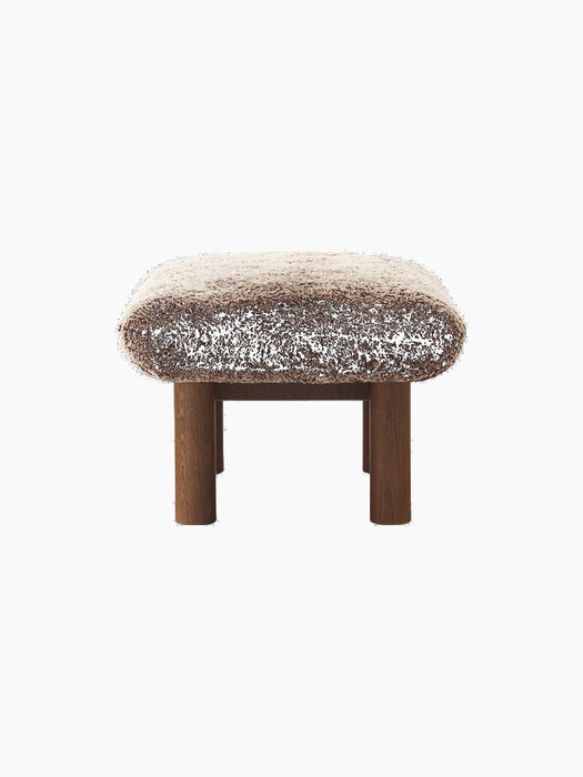 Side view of the Brasilia Ottoman with a plush Sheepskin Root cushion on a dark stained oak base with cylindrical legs.