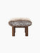 Side view of the Brasilia Ottoman with a plush Sheepskin Root cushion on a dark stained oak base with cylindrical legs.