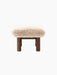 A side profile of the Brasilia Ottoman, showcasing its plush, light brown sheepskin seat atop a robust dark stained oak base.