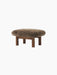 The Brasilia Ottoman with a fluffy brown sheepskin cushion on a dark stained oak base with four thick, cylindrical legs.