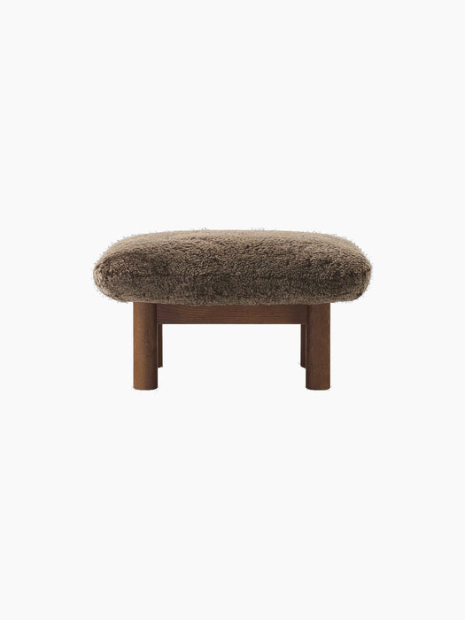 Front view of the Brasilia Ottoman in Sheepskin, with a dark stained oak frame and thick cylindrical legs.