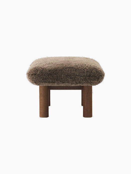 Side view of the Brasilia Ottoman in brown sheepskin, featuring a dark stained oak frame with four robust, cylindrical legs.