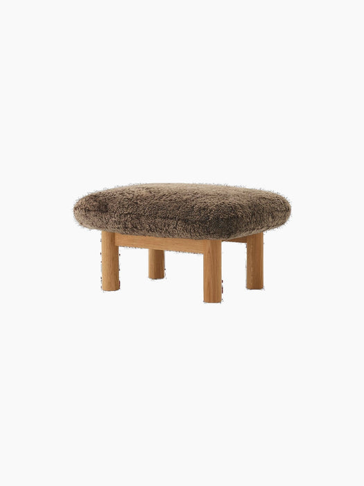 An angled shot of the Brasilia Ottoman, featuring a soft brown sheepskin cushion and natural oak frame with four round legs.