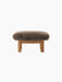 A front view of the Brasilia Ottoman, featuring a plush, brown sheepskin cushion atop a natural oak frame with robust legs.