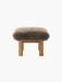 Side profile of the Brasilia Ottoman, featuring a thick, brown sheepskin cushion and robust cylindrical legs in natural oak.