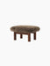 The Brasilia Ottoman in walnut wood with a brown sheepskin upholstery, seen from an angle against a black background.