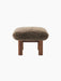 Side view of the Brasilia Ottoman, featuring a plush brown sheepskin cushion and robust, cylindrical legs in walnut wood.
