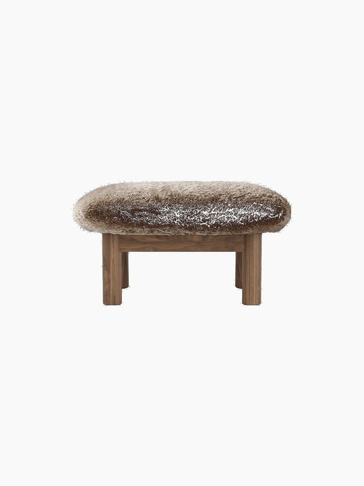 Brasilia Ottoman in Sheepskin, seen from the back. A thick, brown sheepskin seat on a wooden frame with four legs.
