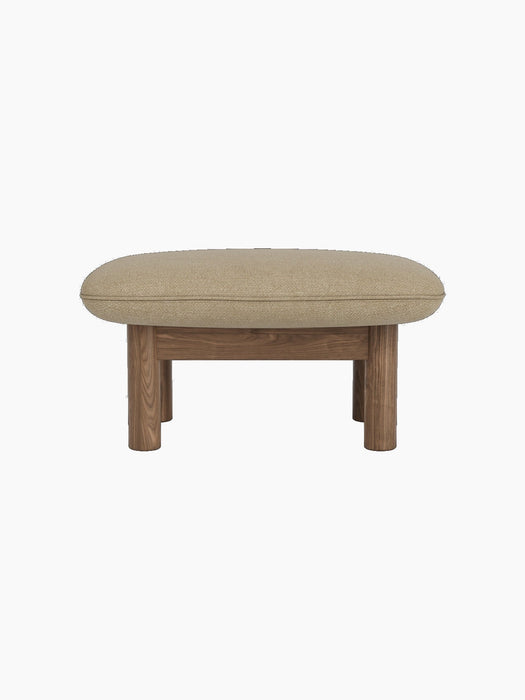 Side view of the Brasilia Ottoman with a walnut frame, thick cylindrical legs and a light beige Audo Bouclé 02 cushion.