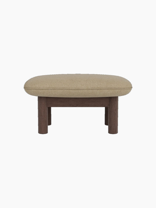 Side view of the Brasilia Ottoman with a dark stained oak frame, robust cylindrical legs and soft Audo Bouclé 02 top.