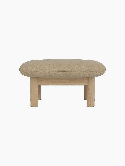 Side view of the Brasilia Ottoman with a light beige Audo Bouclé 02 cushion on a natural oak frame with thick, round legs.