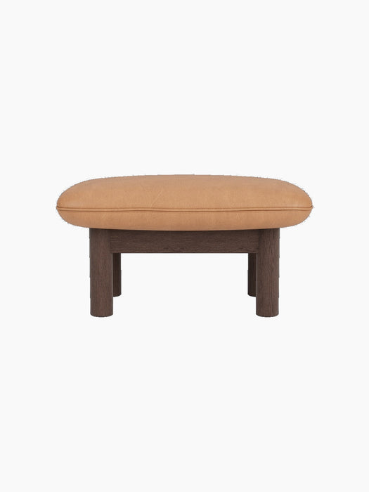 A side view of the Brasilia Ottoman, with a dark stained oak frame, four cylindrical legs, and plush camel leather seat.