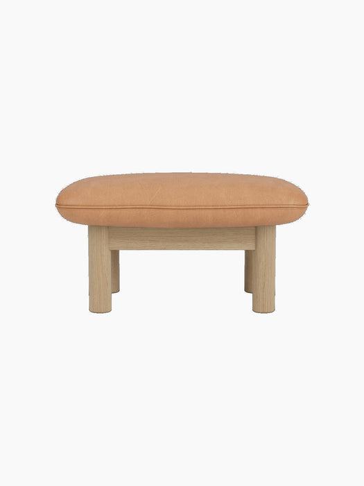 Side view of the Brasilia Ottoman with a camel leather cushion and a natural oak frame with four robust, cylindrical legs.